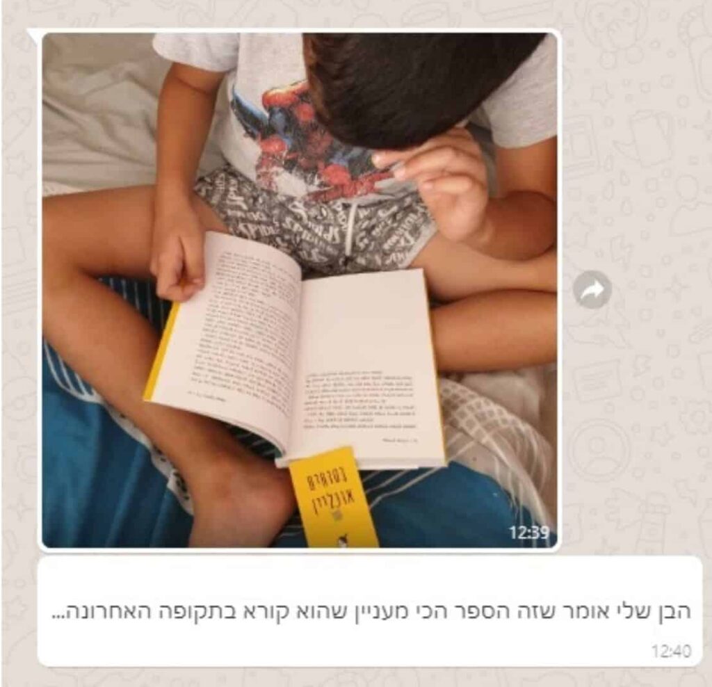 ילד יושב ברגליים משוכלות על משטח כחול, קורא ספר בעברית. הילד מחזיק את הספר פתוח, עם סימנייה צהובה לידו.
